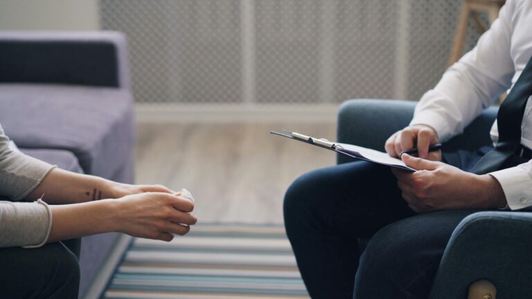 A therapy session with a psychologist and patient, discussing mental health indoors.